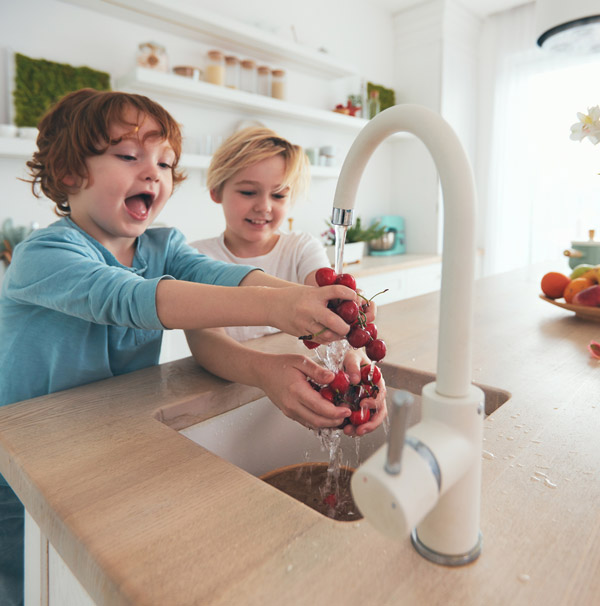 Happy kids washing cherries under tap water at the kitchen.